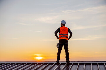 A proud construction worker standing on the roof and looking at twilight. - obrazy, fototapety, plakaty
