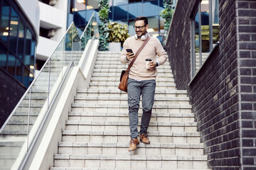 A city man descending the stairs outside and smiling at the phone.