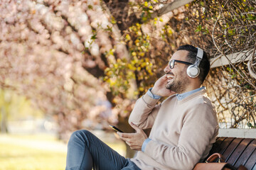 A happy man sits in a park and enjoying music.