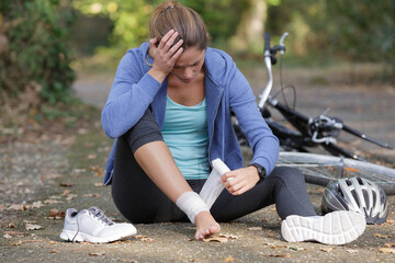 young woman bandaging her ankle after painful fall - obrazy, fototapety, plakaty
