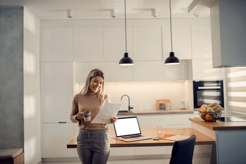 A happy entrepreneur standing in kitchen and working on paperwork.