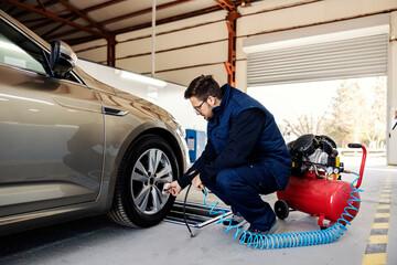 An auto mechanic crouching and preparing to inflate the car tire at garage.