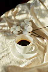 Cup of coffee in bed with cotton flowers,  morning mood, Organic and natural linen cotton textile bedclothes, copy space.