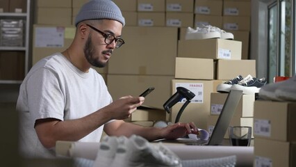 Asian man online seller confirming orders from customer on the phone. E-commerce business owner looking at the phone in store warehouse.