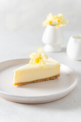 Classic New York cheesecake with fresh vanilla flower on white concrete background, side view. A piece of Vanilla cheesecake on a white plate. Confectionery menu, recipe. Close up. Vertical