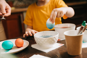 Easter day. Male Father and son painting eggs on wooden background. Family sitting in a kitchen. Preparing for Easter, creative homemade decoration. Child kid boy having fun and painting easter eggs
