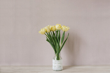 Yellow tulips in a glass vase on a wooden table against a wall background. Copy space