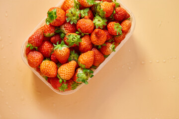 Red ripe organic strawberries in plastic tray container on orange background, copy space for text, top view, market local farm concept, harvest.