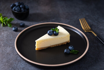 New York cheesecake or classic vanilla cheesecake with fresh blueberries and mint on dark stone background. Side view, close up. Menu, recipe, confectionery