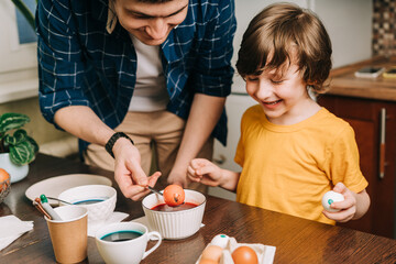 Easter day. Male Father and son painting eggs on wooden background. Family sitting in a kitchen....