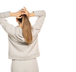 a young woman in a gray tracksuit ties a pony tail to a white background in the studio