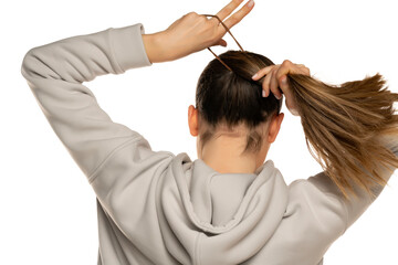 a young woman in a gray tracksuit ties a pony tail to a white background in the studio