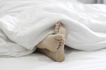 Soles of young women's feet on the bed and white blankets