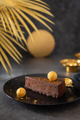 Raw vegan chocolate vanilla cheesecake with golden truffle on dark background. Side view, copy space. Bakery, confectionery menu. No bake chocolate mousse dessert recipe