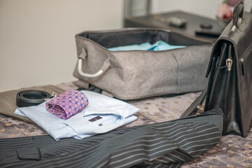 Packing suitcase for business travel. Clothes and briefcase on the bed.
