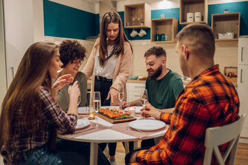 Group of friends enjoying dinner while sitting at the kitchen table together