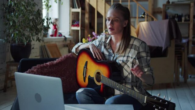 A woman finds a guitar lesson on the Internet and tries to hold the guitar