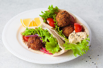 Falafel pita sandwich with fresh vegetables and hummus on white plate. Vegan food concept.