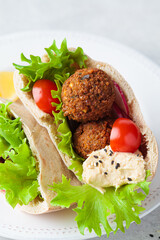 Falafel pita sandwich with fresh vegetables and hummus on white plate. Vegan food concept.