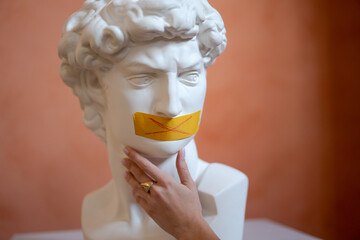 Replica head statue antique statue David, mouth is sealed with yellow tape, against the background...