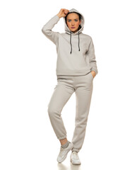Front view of a young woman in a gray tracksuit and hood posing to a white background in the studio