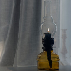 Fototapeta na wymiar Kerosene lamp on the windowsill.Delicate tulle on the windowsill and a kerosene lamp.