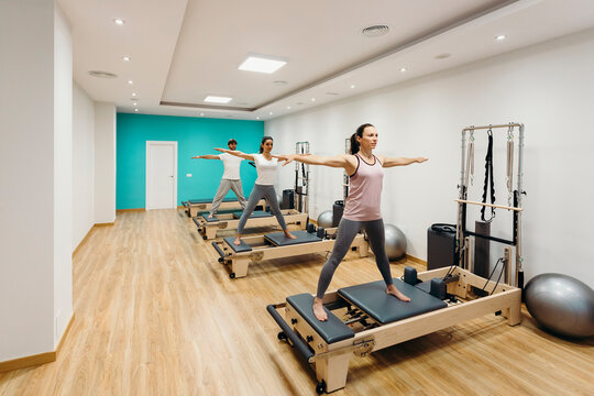 Man and women with arms outstretched exercising on reformer equipment in studio