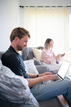 Freelancer working on laptop with woman using mobile phone at home