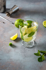 Mojito cocktail. Glass of cold mohito beverage with lime, leaves of mint, bar accessories on dark grey background with copy space. Cocktail bar Weekend or holiday party, menu, recipe