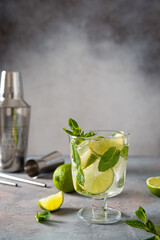 Fresh Mojito cocktail. Glass of cold mohito beverage with lime, leaves of mint, bar accessories on dark grey background with copy space. Cocktail bar Weekend or holiday party, menu, recipe