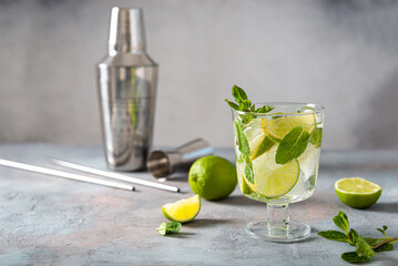 Mojito cocktail. Glass of cold mohito beverage with lime, leaves of mint, bar accessories on dark grey background with copy space. Cocktail bar Weekend or holiday party, menu, recipe