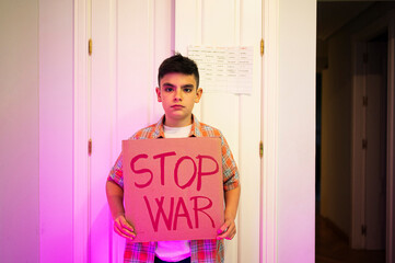 Boy with stop war placard standing in front of door at home