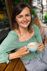 Cheerful young woman having coffee at the cafe outdoors