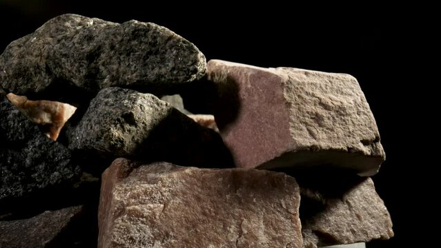 Pieces of solid rough granite stone rotating against a black studio background. Brown and gray granite or quartz minerals. Stones for construction. Geology, ore, resources. Natural stones close up.