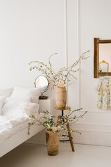 Spring tree branches with white flowers in vases in the interior of a white bedroom in Scandinavian style