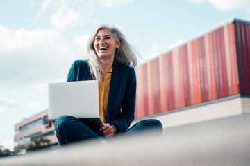 Happy businesswoman laughing sitting with laptop at office park