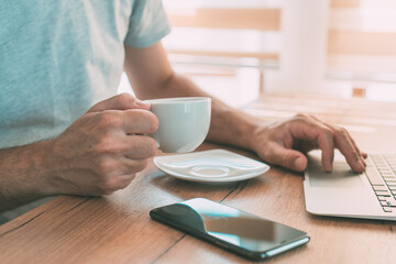 Freelancer is drinking coffee and working from home on laptop computer in the morning