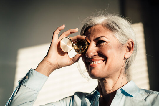 Smiling businesswoman covering eye with navigational compass in office
