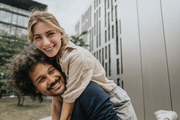 Smiling young man piggybacking girlfriend in front of modern building