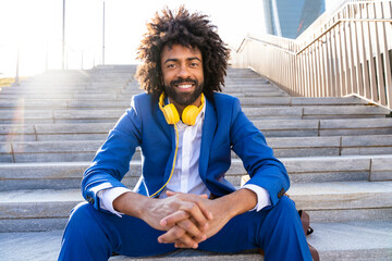 Smiling businessman with headphones sitting hands clasped on staircase