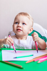 cute little artist draws in an album with pencils, sitting at a small table.