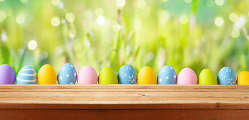 Easter holiday background with empty wooden table and Easter eggs over green grass meadow.  Spring...