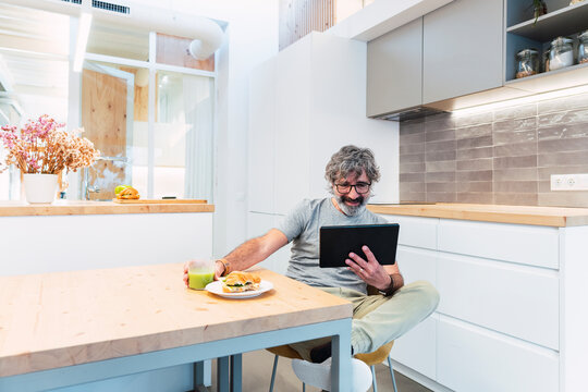 Man sitting at table using tablet PC and having breakfast at home