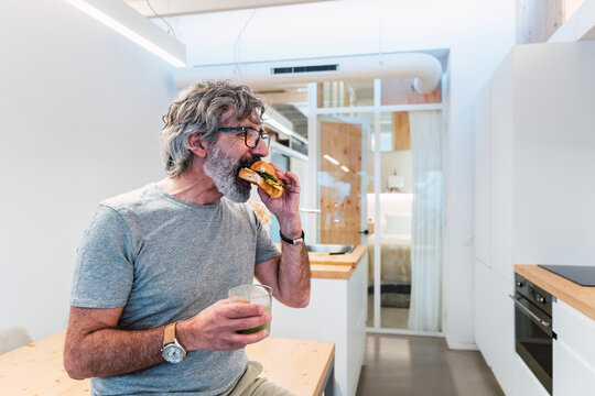 Man eating croissant sandwich with smoothie at home