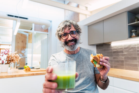 Happy man with croissant sandwich and smoothie at home