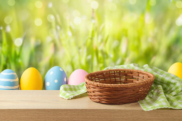 Empty basket with tablecloth and Easter eggs on wooden table over green bokeh background. Easter...