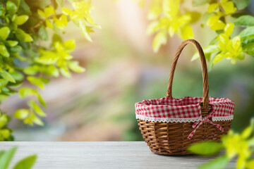Empty picnic basket on wooden table over green leaves background. Spring and easter mock up for...