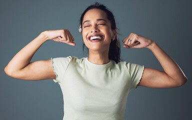 Yes Im a female and no Im not weak. Studio shot of a young woman flexing against a grey background.