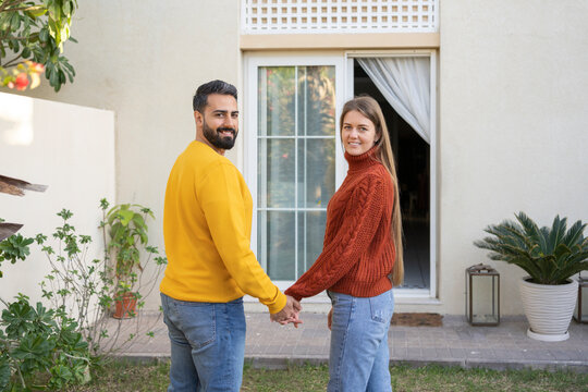 Smiling heterosexual couple holding hands standing in back yard