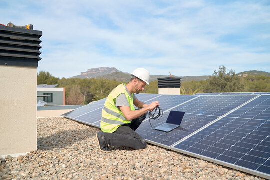 Engineer with laptop and cable installing solar panels on rooftop